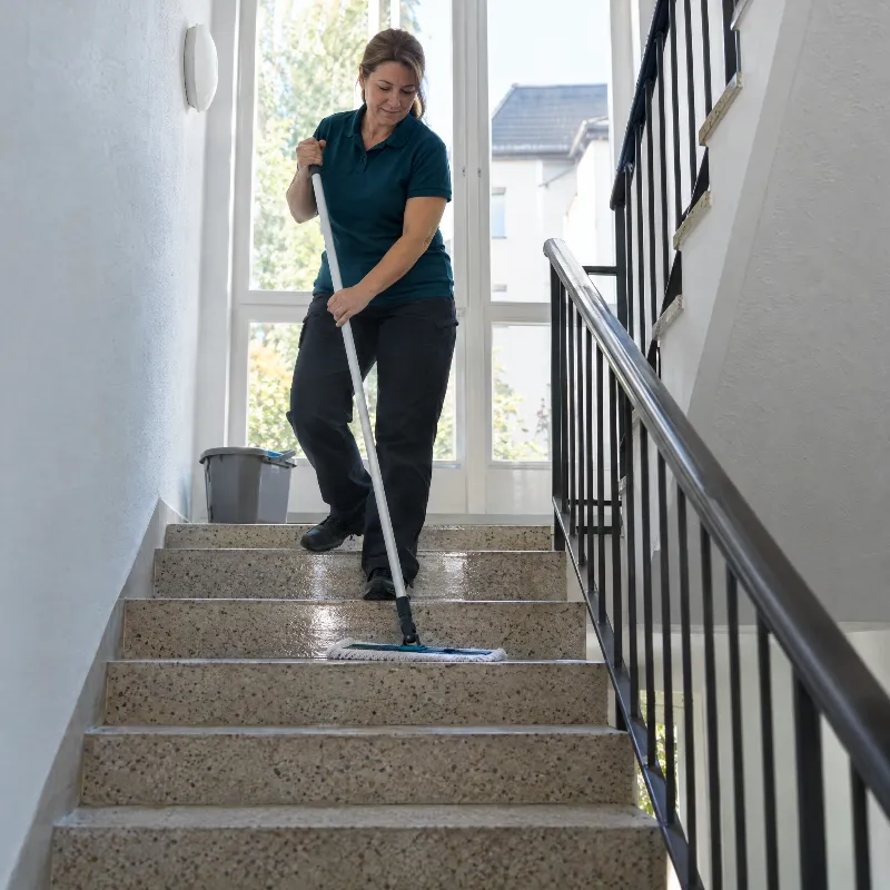 Reinigungskraft wischt ein helles Treppenhaus